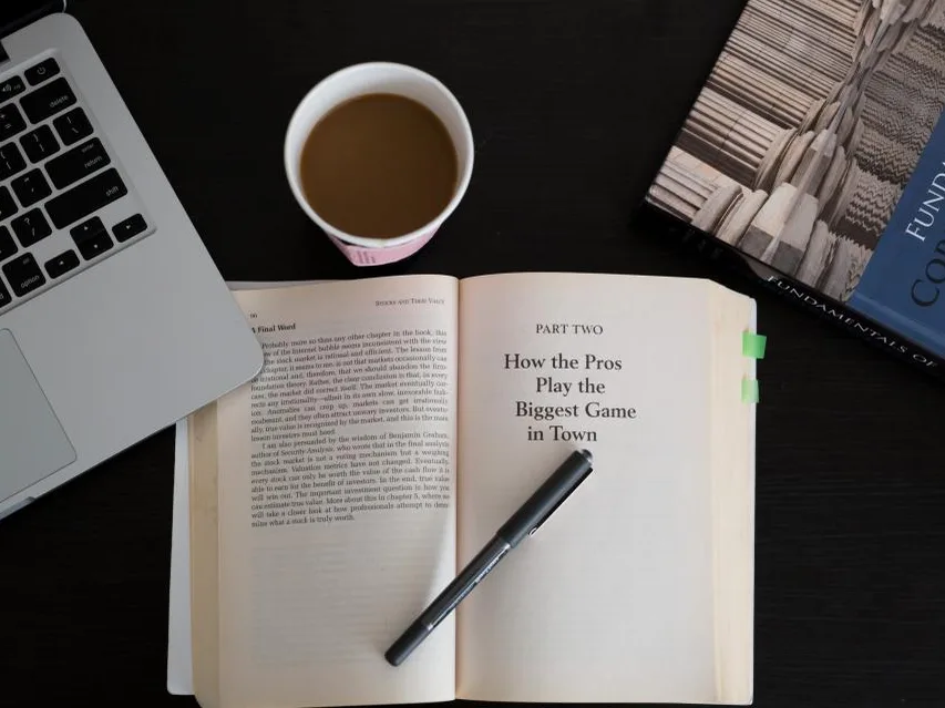 Libro abierto junto a un notebook y una taza de café